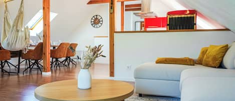 A cozy living room with a round wooden table, a white sofa with mustard pillows, and a hanging chair.