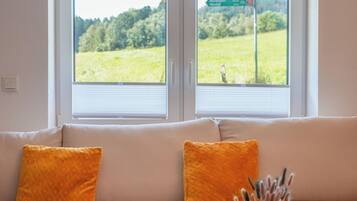 Ein Zimmer mit einer Couch, die zu einem Fenster mit Blick auf ein grünes Feld und einen Wegweiser blickt.