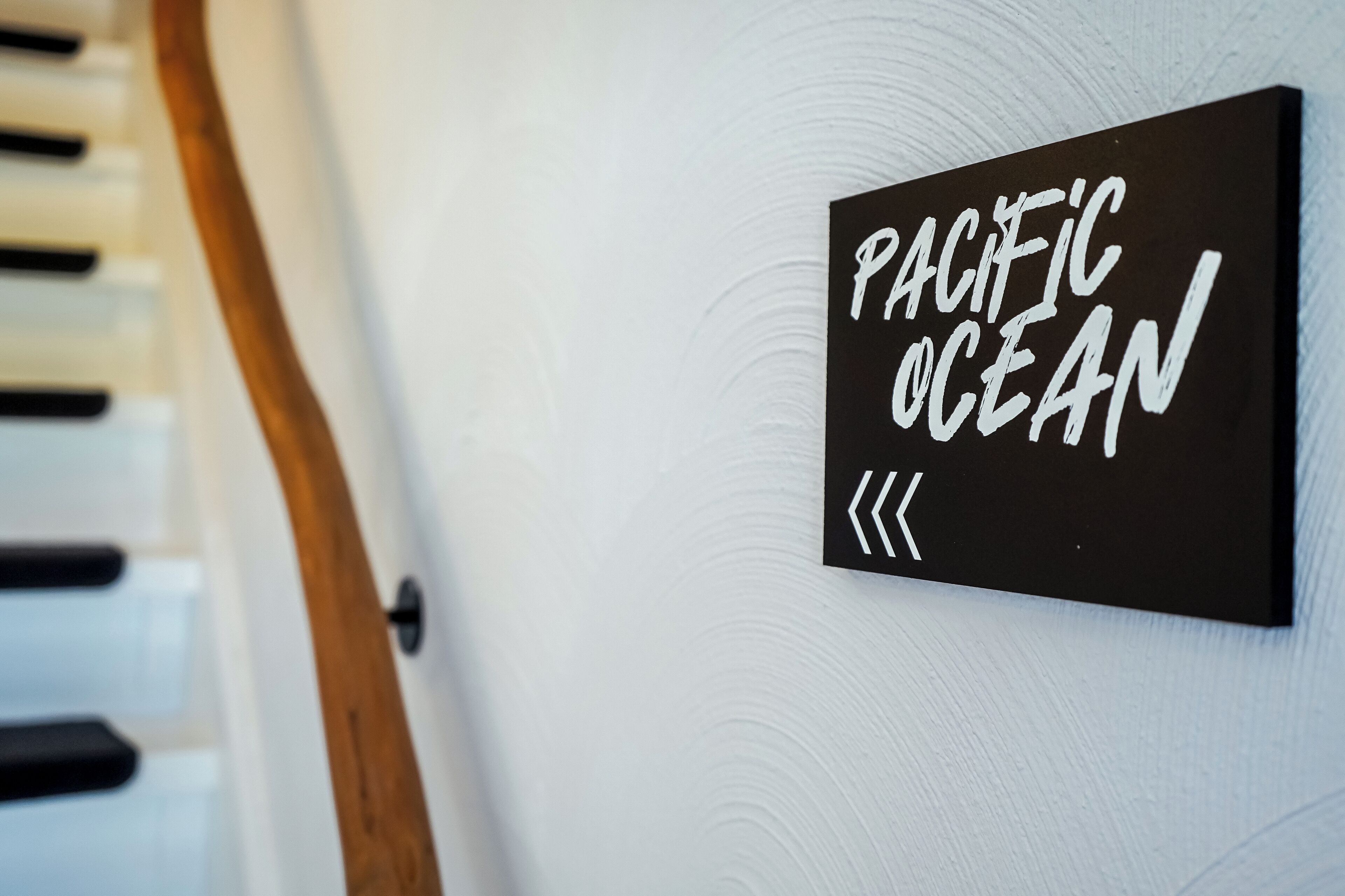 Ein schwarzes Schild mit weißer Schrift, die „PACIFIC OCEAN“ zeigt, an einer weißen Wand.