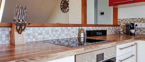 A modern kitchen with a wooden countertop, stainless steel appliances, and a clock on the wall.