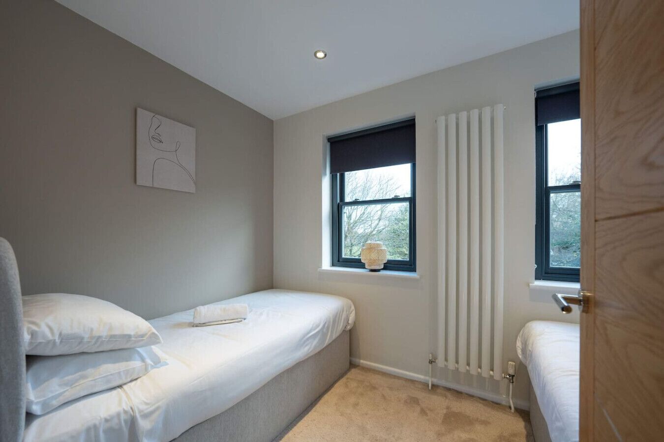 A bedroom with two single beds, a radiator, a window with curtains, and a wall-mounted artwork.
