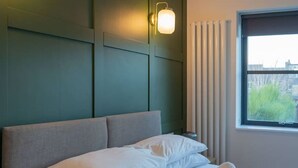 A neatly made bed with white linens, a grey headboard, and two wall-mounted light fixtures.