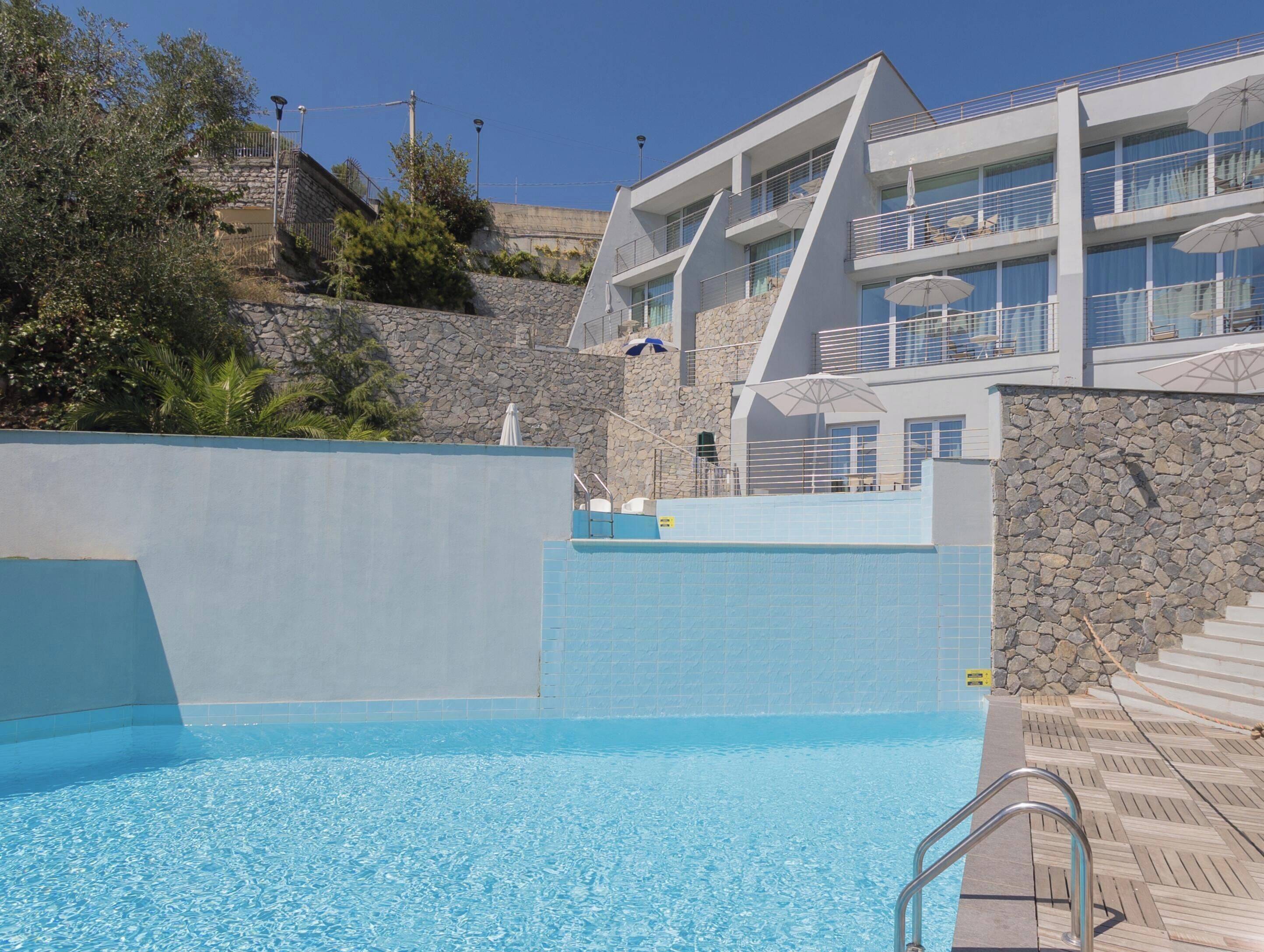 Une piscine bordée d’un mur en pierre et un bâtiment moderne doté de balcons.