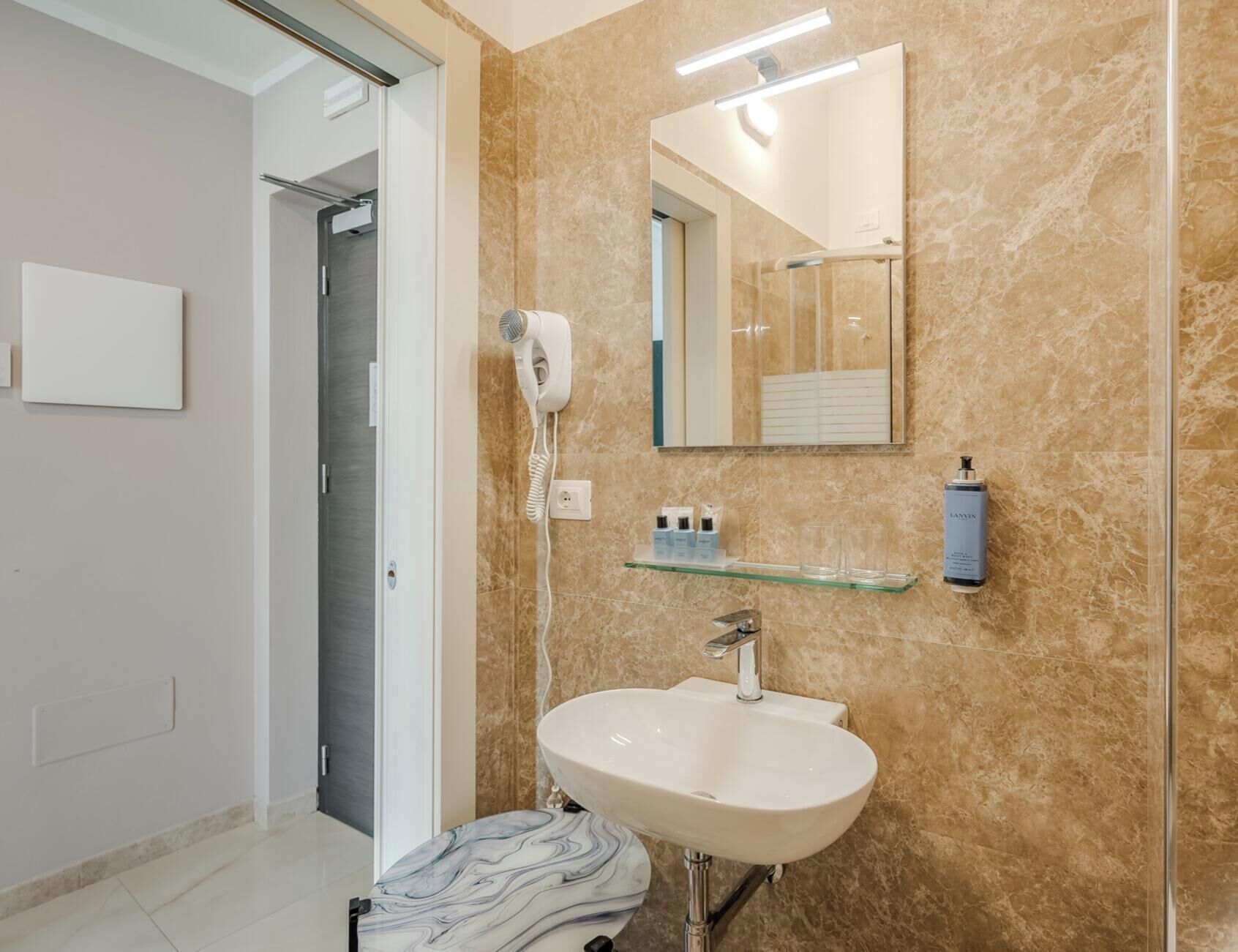 Un baño con pared de mármol, lavamanos blanco, secador de pelo y espejo.
