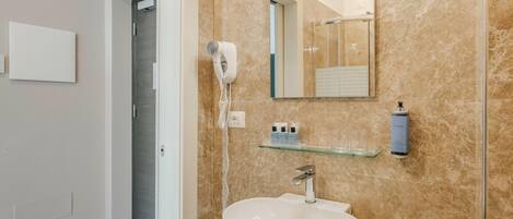 Un baño con pared de mármol, lavamanos blanco, secador de pelo y espejo.
