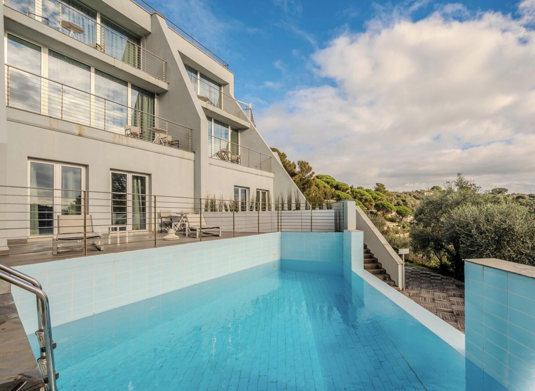Un edificio moderno con piscina, mobiliario exterior y una escalera que lleva a un balcón.