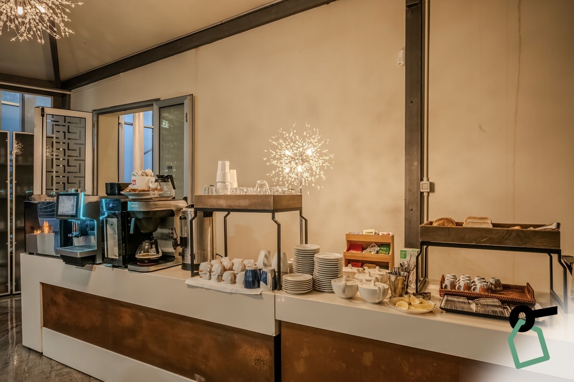A buffet setup with a coffee machine, plates, cups, and various food items.