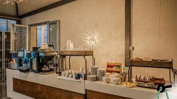 A buffet setup with a coffee machine, plates, cups, and various food items.