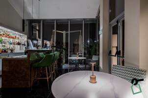 Uma área de bar moderna com um expositor de vidro cheio de garrafas, banquetas de bar verdes e uma mesa redonda com uma vela.