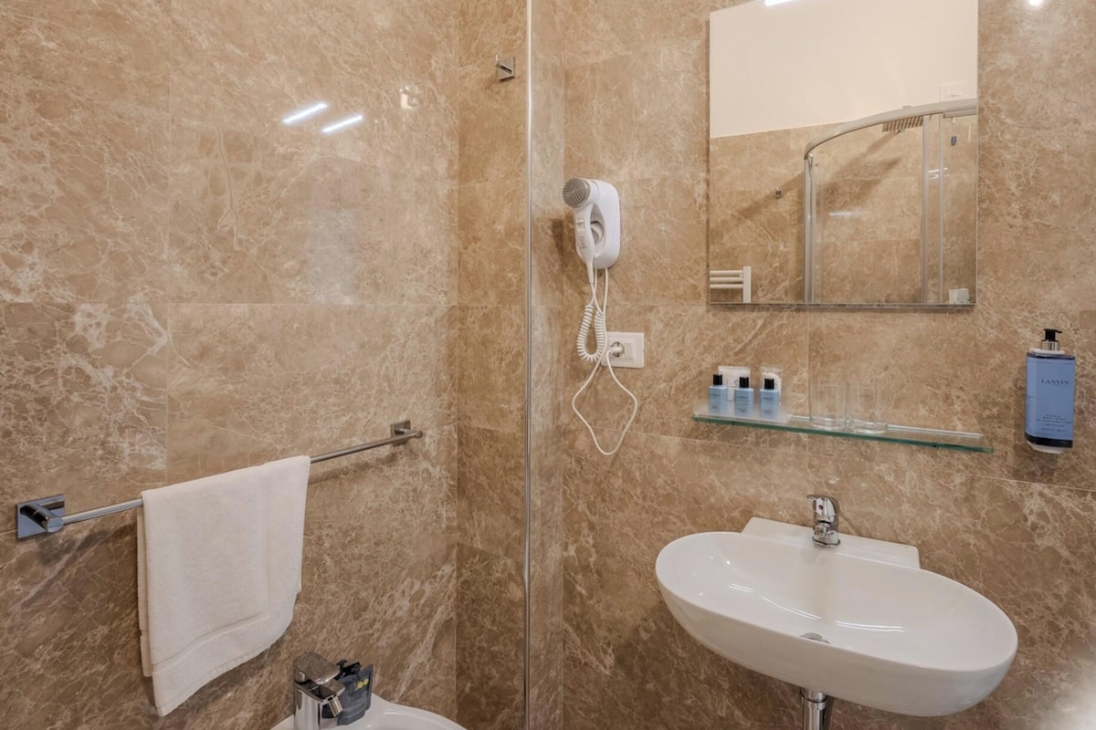 A bathroom with a marble wall, a glass shower enclosure, a white sink, and a towel rack.