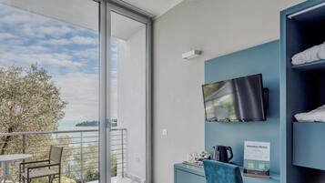 Quarto de hotel com varanda, televisão de tela plana na parede, escrivaninha com chaleira e placa indicando o tipo de quarto.