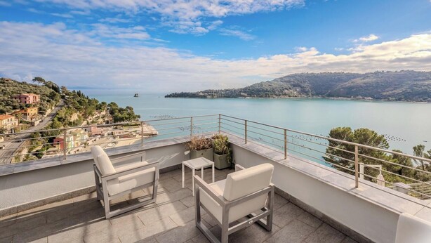 Una terraza con vistas a un lago y colinas distantes, amueblada con sillas blancas y una pequeña mesa.