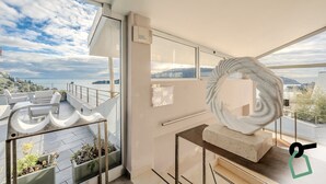 Un interior moderno con grandes ventanales, vista al mar y una decoración minimalista que incluye una escultura y un bloque de hormigón.