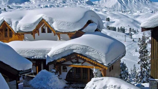 A snow-covered lodge with wooden architecture, a ski slope in the background, and a clear blue sky. - lesetoilesdelaplagne.com les montagnettes foot slopes (La Plagne-Tarentaise)