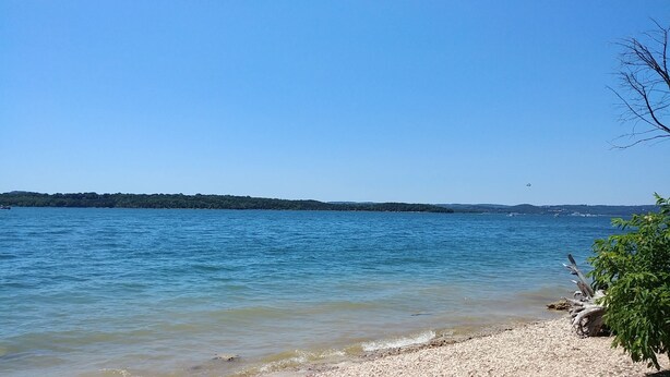 On peut clairement voir un lac, avec une rive de galets et une terre ferme qui s’étend au loin.