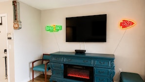 Un salon avec une commode turquoise, un téléviseur à écran plat, une cheminée, un tapis à motifs et des enseignes lumineuses néon représentant la distillerie « Buffalo Trace » et l’équipe de football américain des « Kansas City Chiefs ».