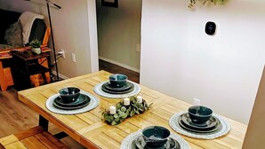 Un espace repas avec une table en bois dressée pour quatre personnes, des bancs et un luminaire suspendu.