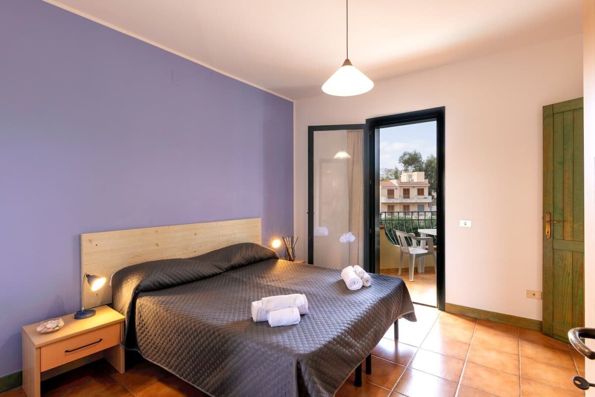 Ein Schlafzimmer mit Bett, Nachttischlampe und Blick auf den Balkon.
