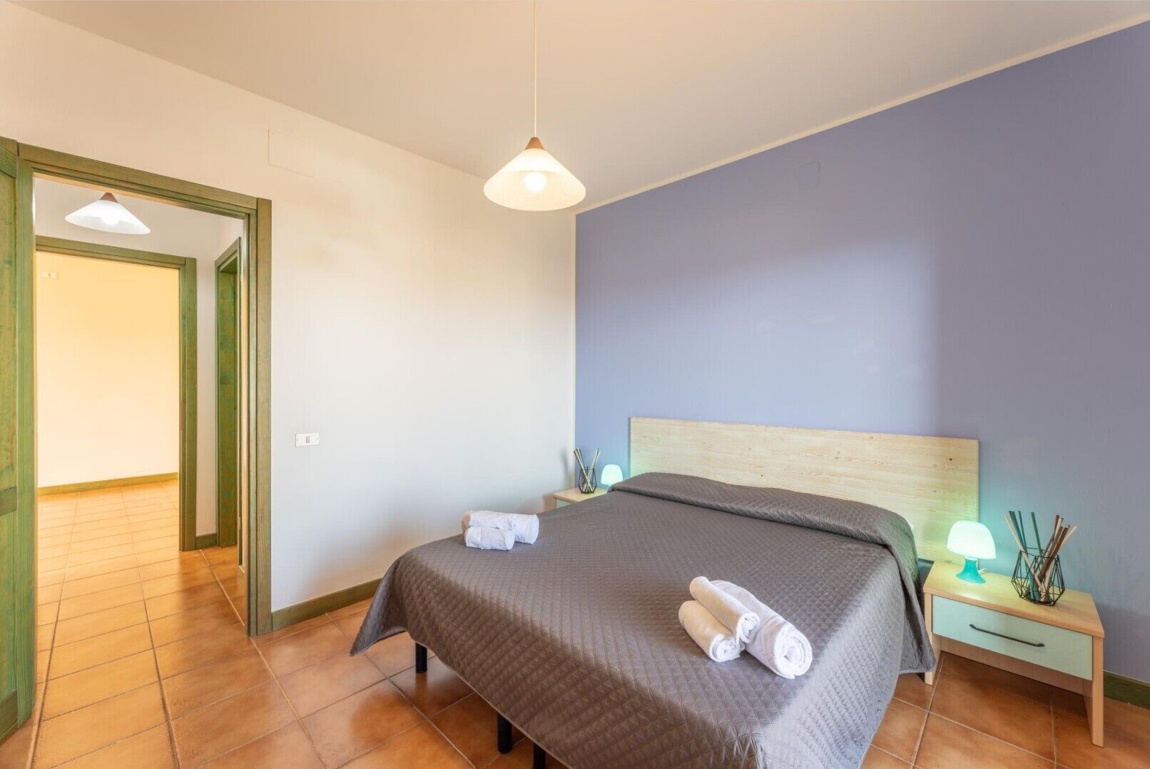 Un dormitorio con cama, mesita de noche, lámpara y puerta que da a otra habitación.