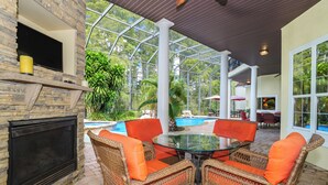 A covered outdoor area with wicker furniture, a glass table, and a fireplace. - Magnificent 8 Bed 8 Bath Custom  6500+ SqFt. Pool/spa. NEW DISCOUNTED 2026 rates (Kissimmee)