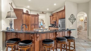 A spacious kitchen with a large island, wooden cabinetry, and bar stools. - Magnificent 8 Bed 8 Bath Custom  6500+ SqFt. Pool/spa. NEW DISCOUNTED 2026 rates (Kissimmee)