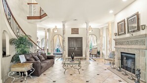 A spacious living room with a fireplace, a staircase, and a large window. - Magnificent 8 Bed 8 Bath Custom  6500+ SqFt. Pool/spa. NEW DISCOUNTED 2026 rates (Kissimmee)