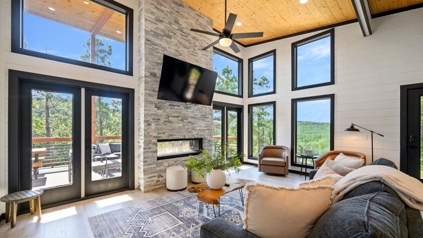 A spacious living room with a fireplace, large windows, and a ceiling fan. - Stargaze from Your Private Hot Tub (Broken Bow)