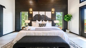 A modern bedroom with a large bed, two bedside tables, wall-mounted lights, a large window, and a potted plant. - Stargaze from Your Private Hot Tub (Broken Bow)