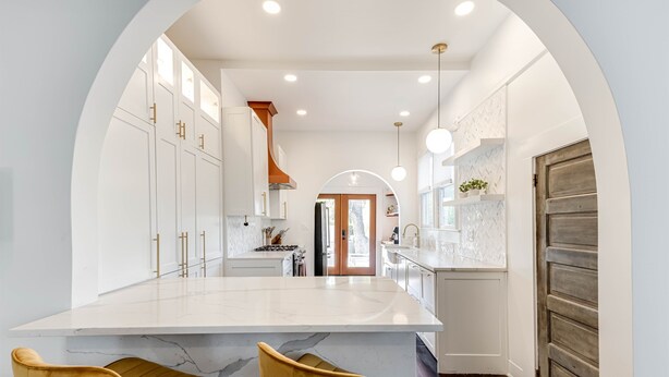 A modern kitchen with white cabinetry, a marble island, and two yellow chairs. - Luxury Retreat Near San Antonio Icons (San Antonio)
