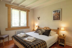A bedroom with a bed, two bedside tables, a chair, a window with curtains, and a wall-mounted picture. - Chalet Léonice - 8 guests - Jacuzzi & Sauna, Gérardmer (Gérardmer)
