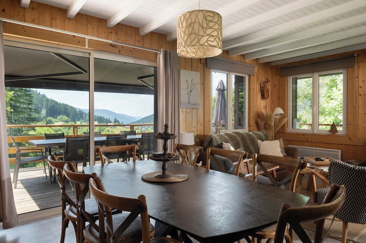 A wooden interior with a large dining table, chairs, and a view of the outdoors.