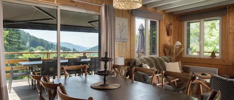 A wooden interior with a large dining table, chairs, and a view of the outdoors.