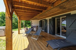 Una terraza de madera con dos sillones de descanso, un sofá y un ventanal corredero que da a un patio.