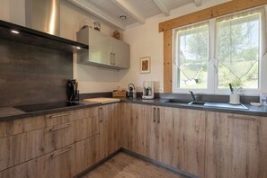 Une cuisine moderne avec des meubles en bois, un plan de travail noir, un four encastré et une fenêtre donnant sur un paysage verdoyant.