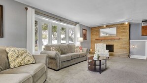 A living room with a sofa, armchair, and coffee table. There is a fireplace with a mirror above it. - Comfort and Space near MSU (Lansing)