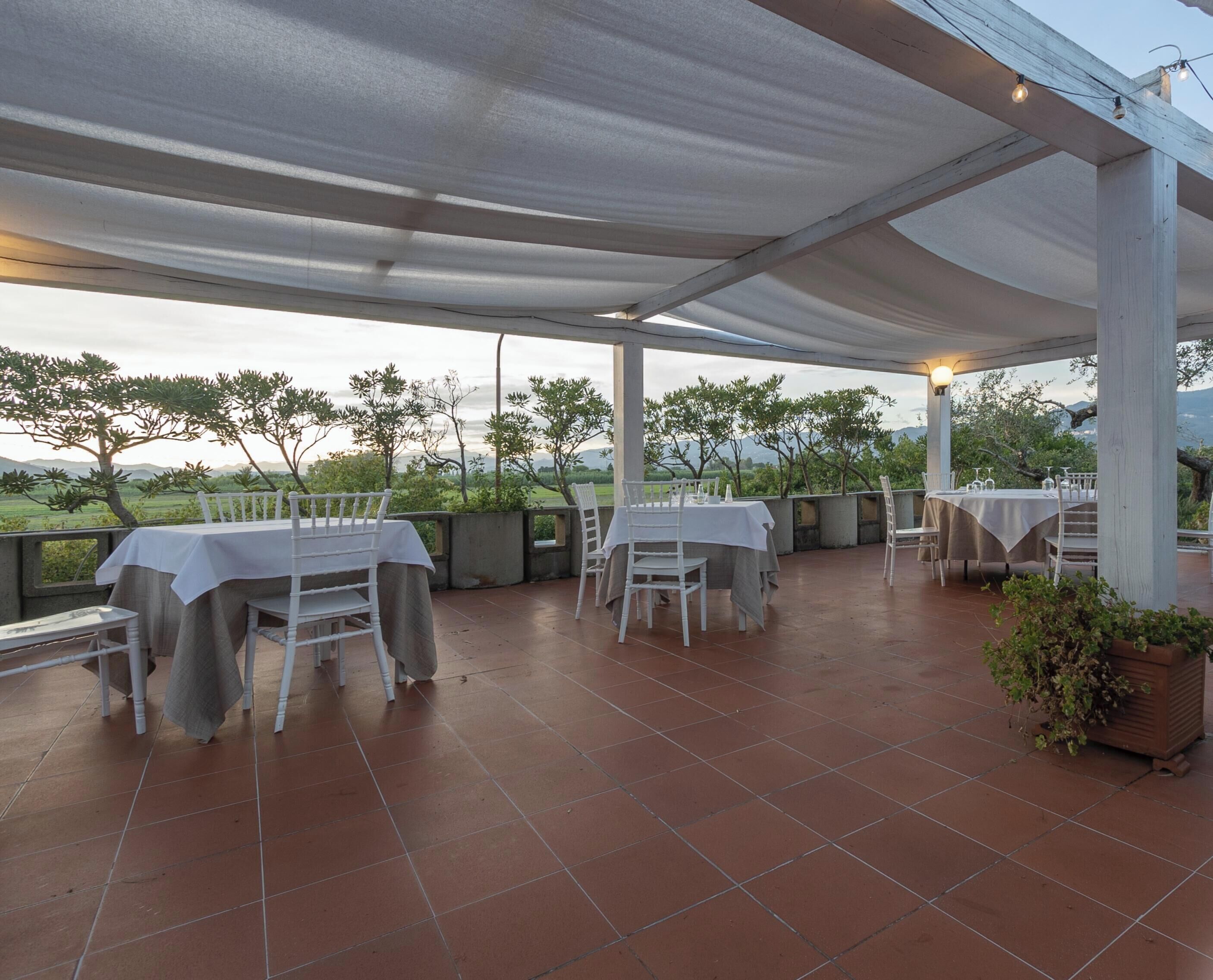An outdoor patio with tables and chairs, a pergola overhead, and a view of the landscape.