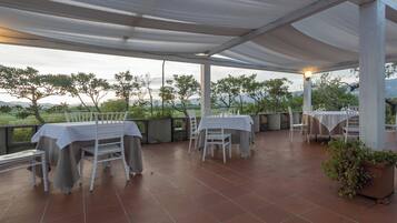 An outdoor patio with tables and chairs, a pergola overhead, and a view of the landscape.