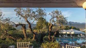 Un área de comedor al aire libre con una mesa dispuesta para dos, con vistas a una piscina y un paisaje montañoso.