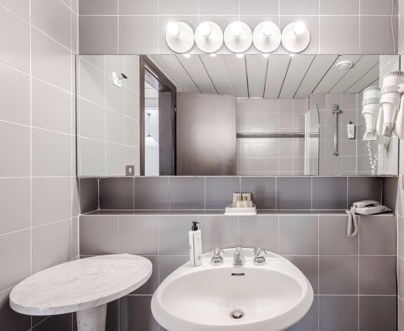 A modern bathroom with a large mirror, a round sink, and a hairdryer on the wall.