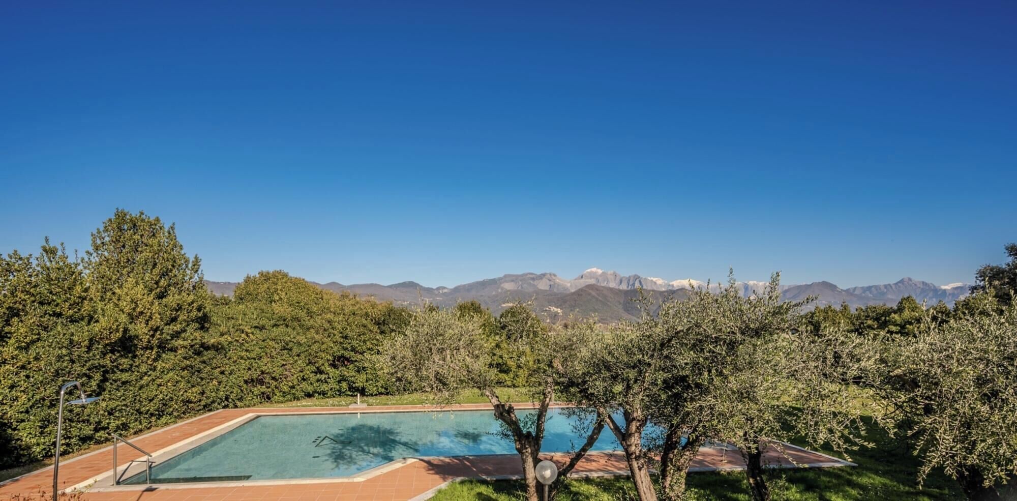 Ein Pool mit Blick auf eine Berglandschaft, umgeben von Bäumen und blauem Himmel.