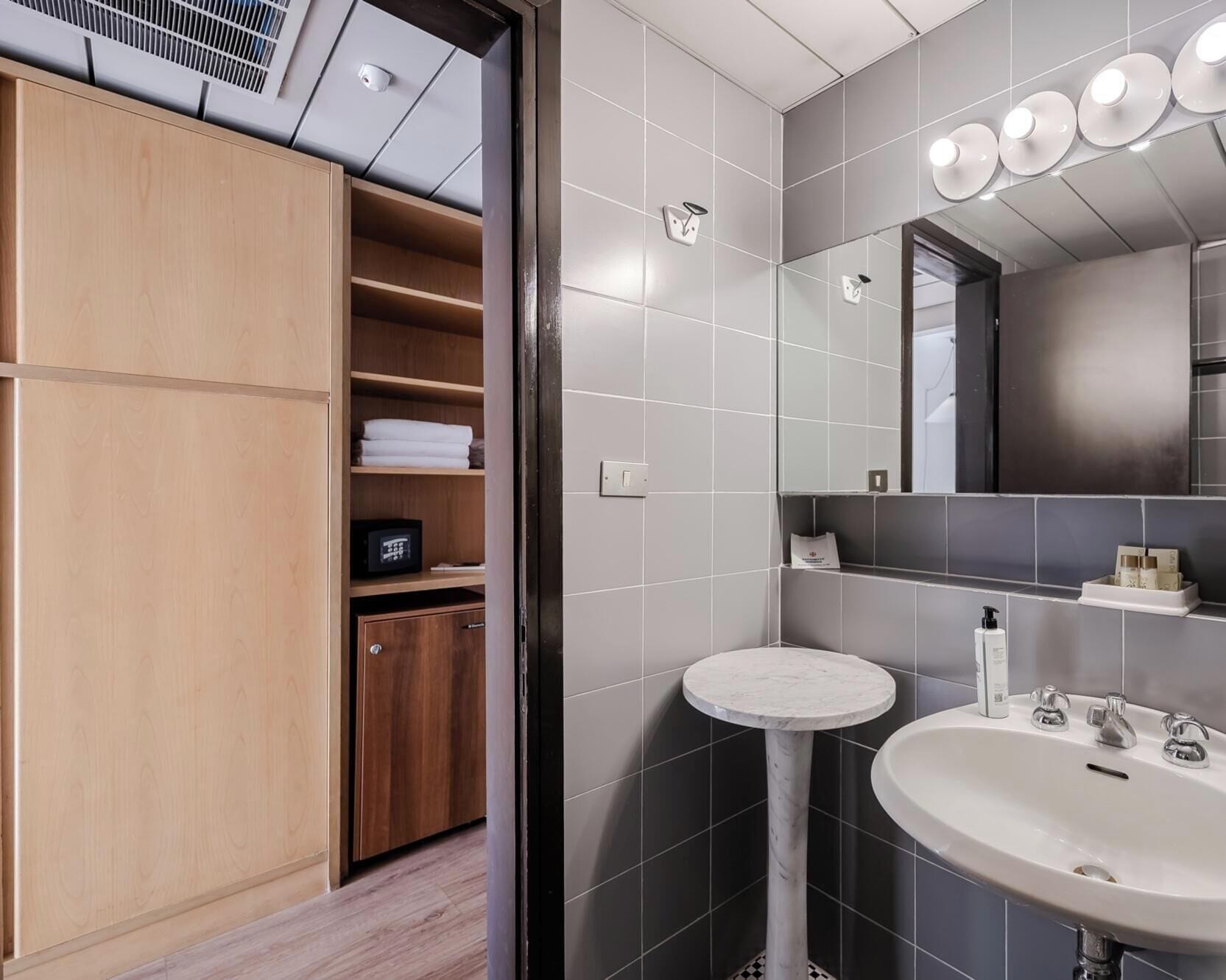 A modern bathroom with a built-in wooden wardrobe, a round marble sink, and a large mirror with lights.