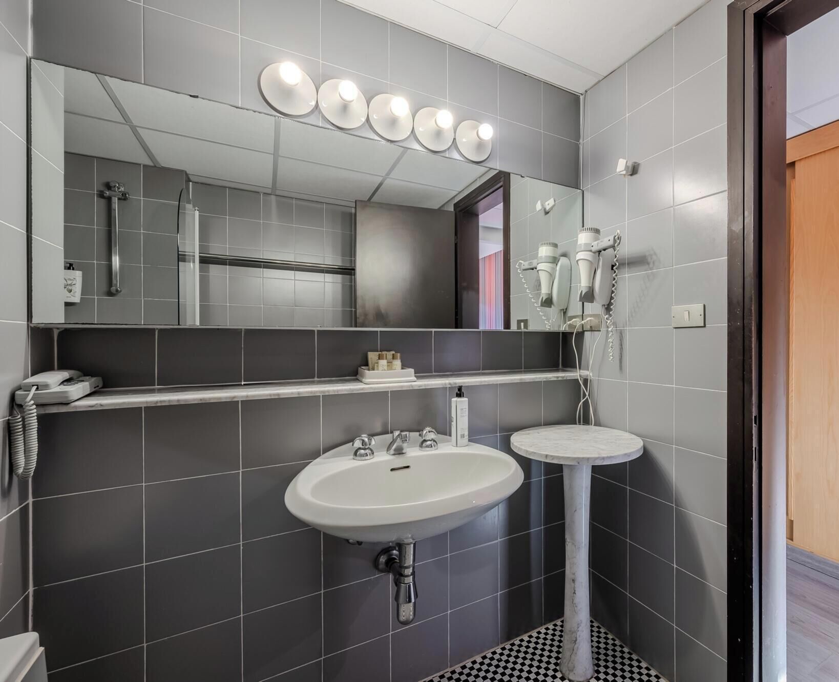 Un baño moderno con un espejo grande, un lavabo y un secador de pelo montado en la pared.