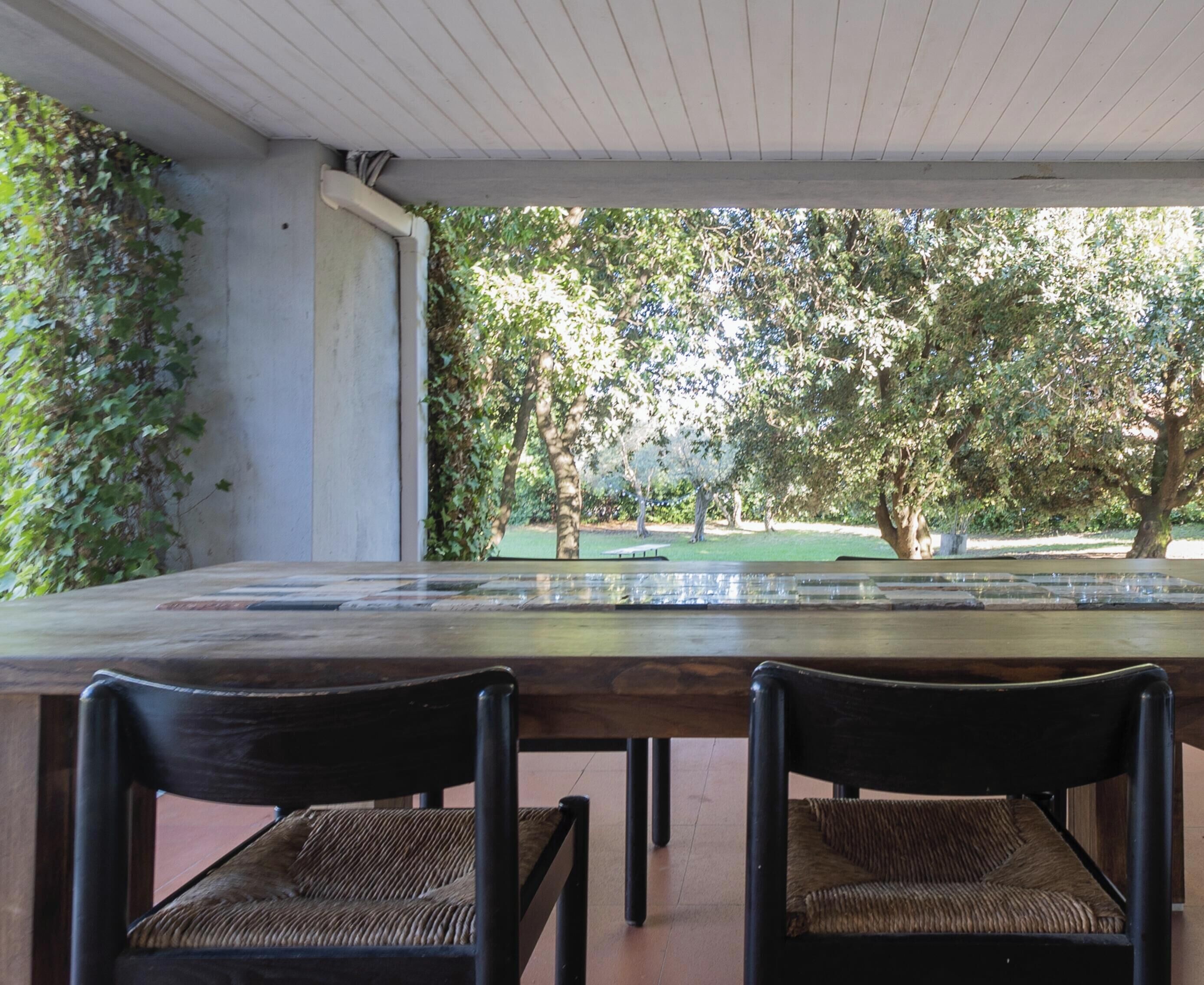 Un comedor con mesa y sillas de madera, vista a un parque con árboles y una fuente.