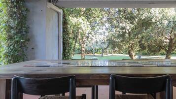 Un comedor con mesa y sillas de madera, vista a un parque con árboles y una fuente.