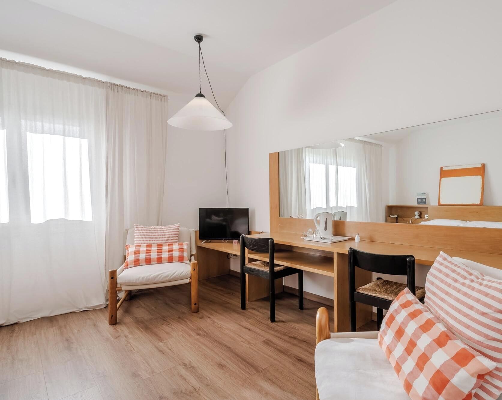 Una habitación con cama, escritorio, silla, televisor y un espejo grande.