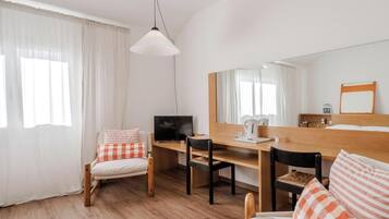 Una habitación con cama, escritorio, silla, televisor y un espejo grande.