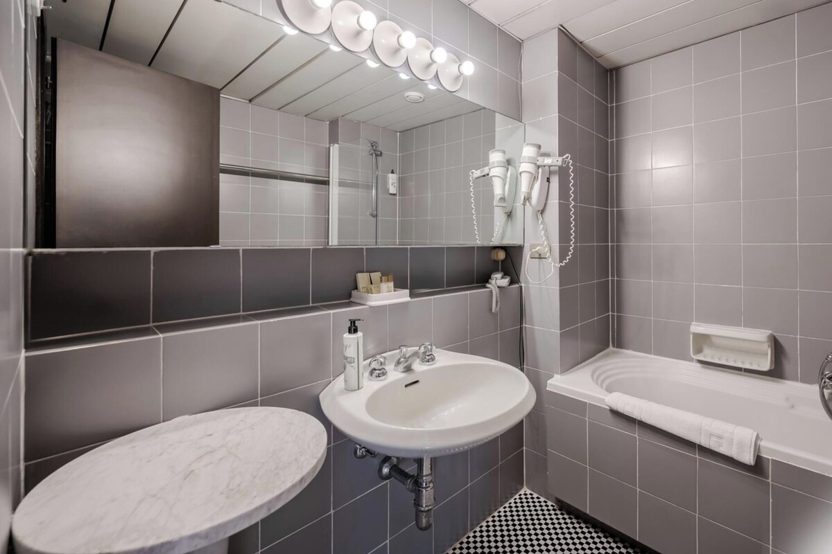 A modern bathroom with a marble sink, a bathtub, and a large mirror with lights.
