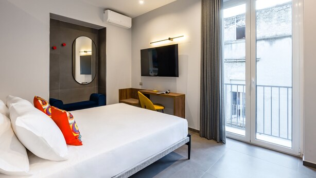 Une chambre d’hôtel moderne dotée d’un grand lit, d’un bureau, d’une télévision et d’un balcon offrant une vue sur la ville.