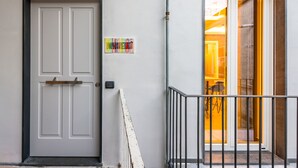 Une porte blanche avec un cadre noir, une petite enseigne avec du texte coloré et un garde-corps en métal menant à un balcon d’où l’on peut admirer l’intérieur.
