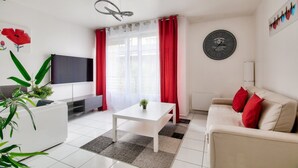 A modern living room with a white sofa, a coffee table, a flat-screen TV, and red curtains.